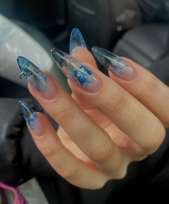 Long almond shaped acrylic clear nails with blue marble nail design and blue butterfly nail art