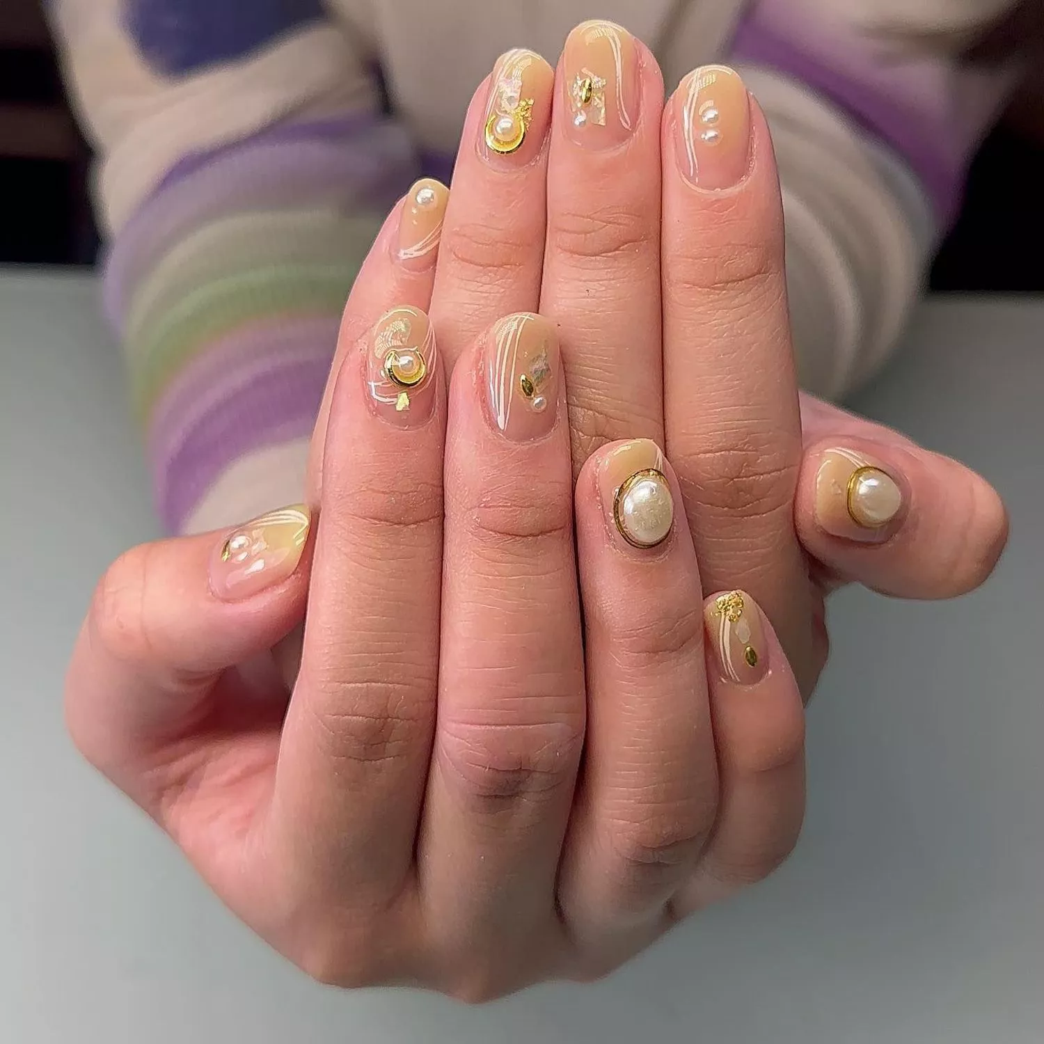 Manicure with shiny neutral base and charm and pearl accents