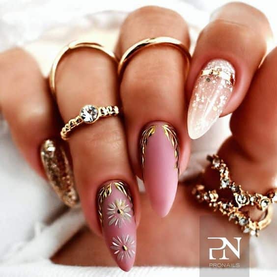 Nude pink nail polish with gold leaves and flower nail art on long almond nails