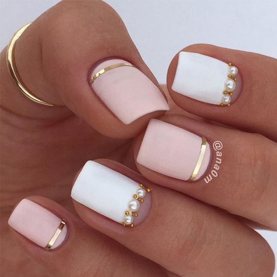 White and light pink nail polish in matte finish with gold lines and pearls on short square nails