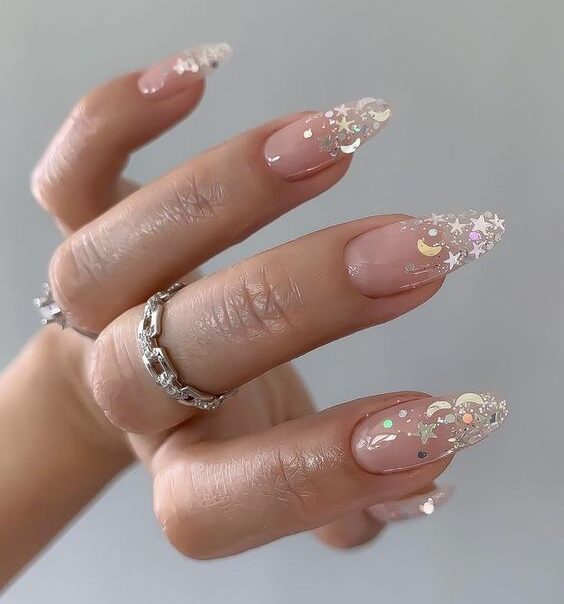 Clear almond shape nails with star and moon shape glitters on the tips