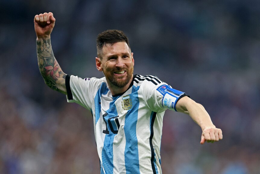 An athletic man wearing a blue and white striped soccer jersey smiles and windmills his fist in front of a large crowd.